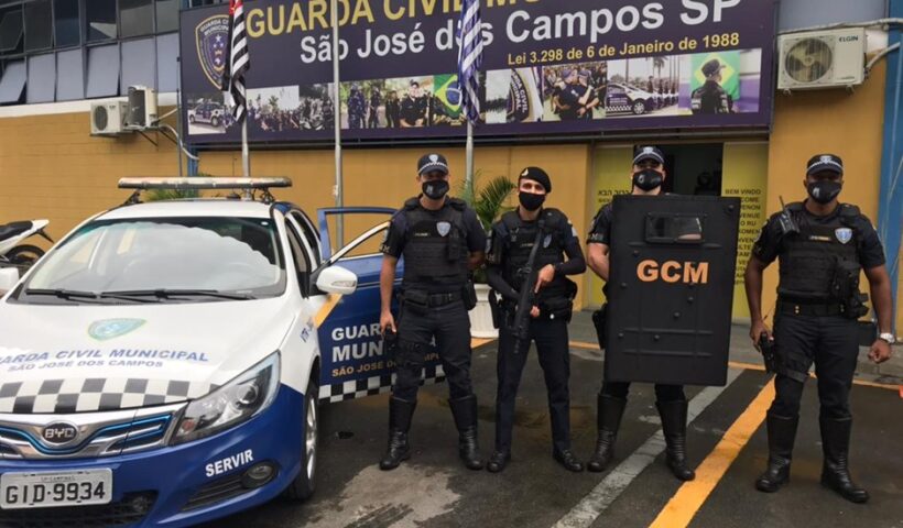 guardas da gcm de são josé em pé, em frente à sede da guarda, uniformizados, com escudo e viatura