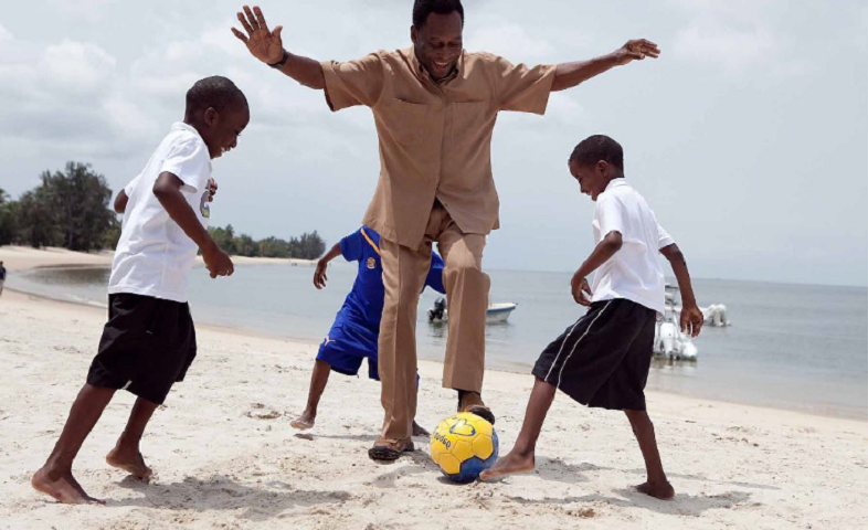 pelé vestido de roupa marrom claro joga bola com três meninos na praia; governos decretaram luto oficial pela morte do rei do futebol