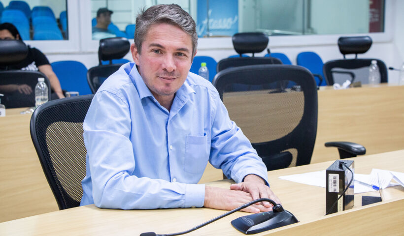 vereador Alberto Barreto, com camisa azul claro, sentado à mesa da camara municipal de taubate, com cadeiras ao fundo, é eleito novo presidente da camara