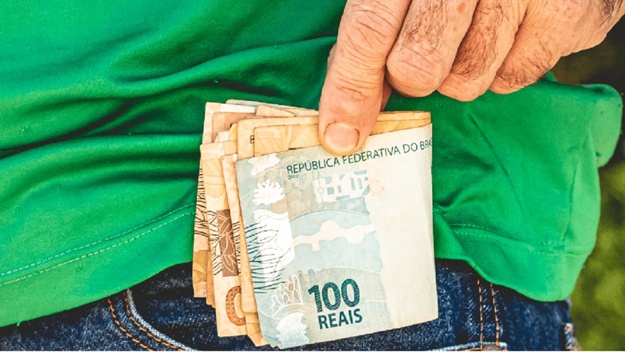 Mão colocando dinheiro no bolso da calça. Mais de 740 mil pessoas têm mais de 1 mil reais esquecidos em contas bancárias