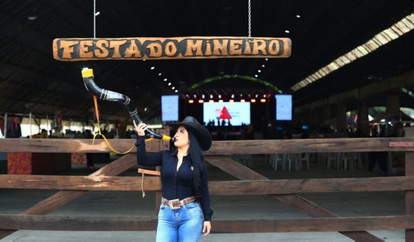 Mulher tocando um berrante, em frente à fachada da Festa do Mineiro, que acontece em São Jose dos Campos anualmente no Parque da Cidade.